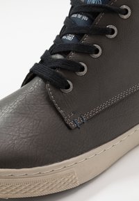 Šedá texturovaná bota s koženým svrškem, černými šňůrkami a kovovými očky. Bílá gumová podrážka s vzorovaným profilem. Výrazné švy.