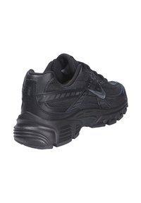 Baskets de sport noires avec une tige en maille texturée et des superpositions en synthétique, dotées d'une semelle en caoutchouc épaisse et d'accents réfléchissants sur le côté.