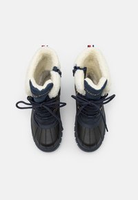 Bottes imperméables navy avec un empeigne en cuir noir, doublure en fausse fourrure blanche et lacets ronds. Œillets en or et semelle texturée.