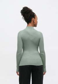 Ριμππλε μακρυμάνικη κορυφή εφαρμοστή σε απαλό πράσινο με ψηλό λαιμό. Το ύφασμα έχει απαλή υφή και καταλήγει σε φαρδύ τελείωμα στη μέση.