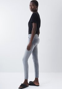 Schwarzes kurzärmeliges Hemd, hellgraue Slim-Fit-Jeans und schwarze rutschfeste Sandalen. Einfaches Design mit glatter Textur und standardmäßiger Naht.