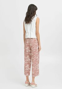Top bianco senza maniche con dettaglio di laccio sul retro abbinato a pantaloni a gamba larga con un motivo a strisce zebrato rosso e bianco.
