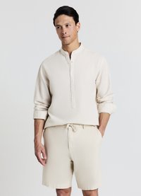 Cream linen shirt with a stand collar and button placket, paired with matching cream shorts. Smooth texture, relaxed fit.