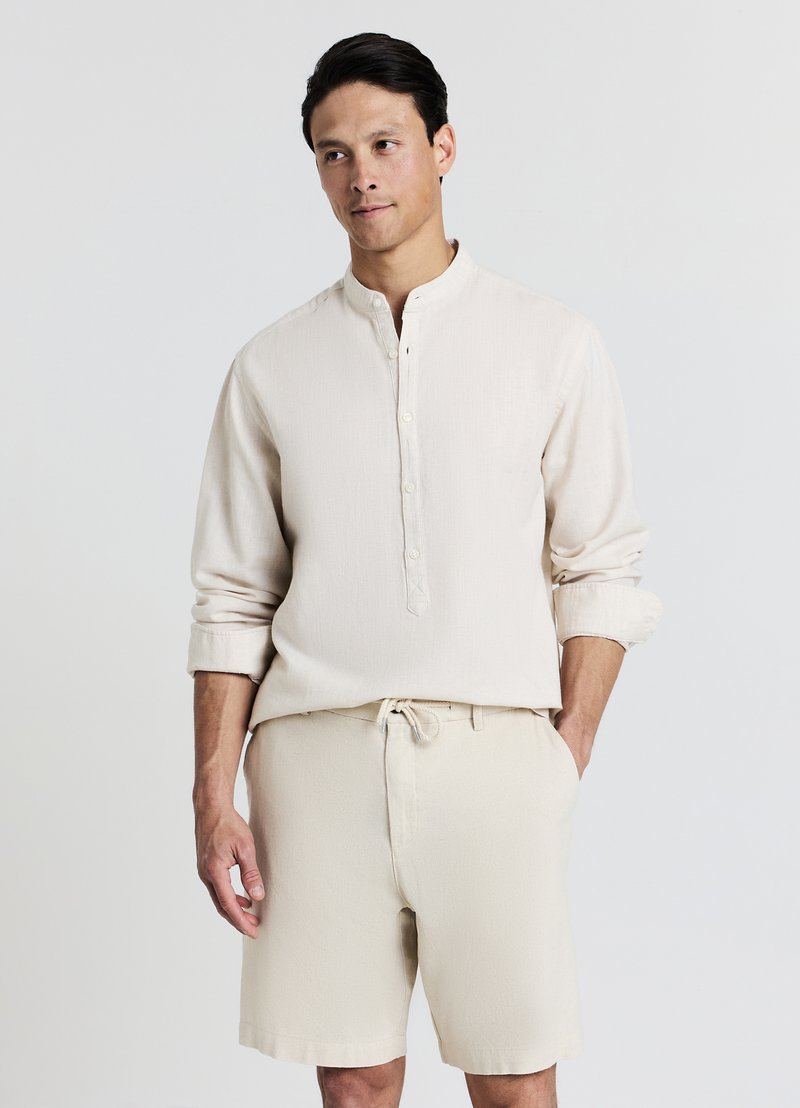 Cream linen shirt with a stand collar and button placket, paired with matching cream shorts. Smooth texture, relaxed fit.