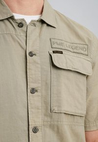 Lys grøn kortærmet skjorte lavet af tekstureret stof, med en brystlomme, knaplukning foran og mærkepatch med "PME LEGEND" tekst.