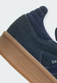 Sneaker con una toma in denim blu scuro, dettagli in suede e una suola in gomma marrone con un motivo di presa testurizzato.