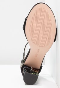 Semelle de chaussure à talon haut noire à motif floral avec talon en caoutchouc rainuré et bande de roulement ondulée sur semelle beige claire, taille 37.