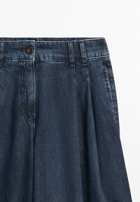 Donkerblauwe denimrok met tailleband, knoopsluiting, riemlussen en zijzakken op een witte achtergrond.