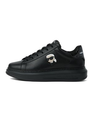 Schwarzer Ledersneaker mit dicker Sohle, schwarzen Schnürsenkeln und einem Cartoon-Gesicht mit Sonnenbrille und weißen Haaren an der Seite.