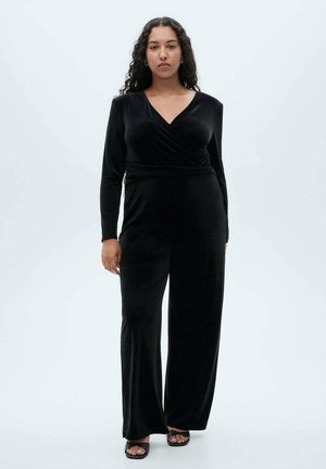 Jumpsuit in velluto nero con maniche lunghe, davanti avvolgente e gambe ampie. Presenta una texture liscia e un drappeggio elegante, offrendo un aspetto aderente.