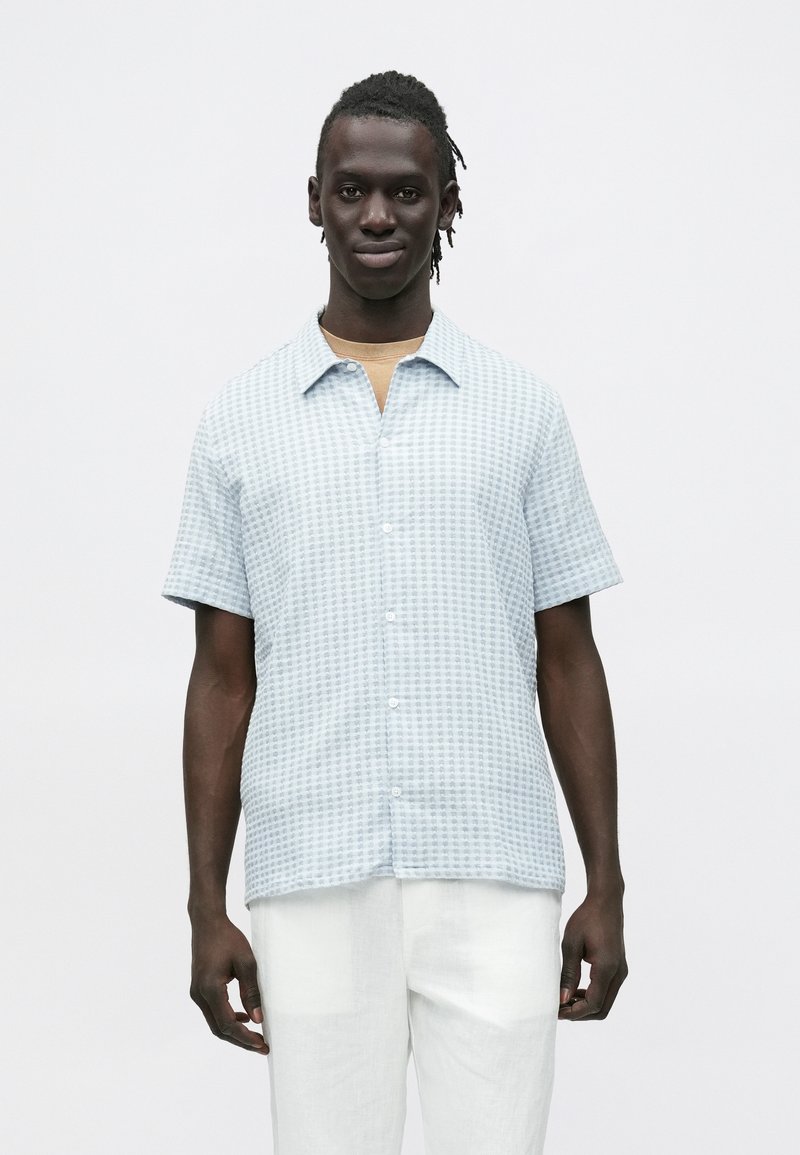 Lichtblauw overhemd met korte mouwen en een geruit motief, met knoopsluiting aan de voorkant en een zachte textuur, gecombineerd met witte linnen broek.