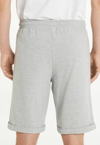 Los pantalones cortos de algodón grises cuentan con una cinturilla elástica, puños enrollados y una textura suave. El diseño es simple y práctico, adecuado para el uso casual.