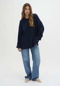 Maritiem oversized sweater met geribbelde manchetten, gecombineerd met lichtblauwe wijde jeans en beige schoenen met een geweven patroon.