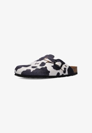 Klapki typu slip-on z czarno-białym wzorem krowy, regulowany pasek z klamrą, korkowa wkładka i czarna podeszwa.