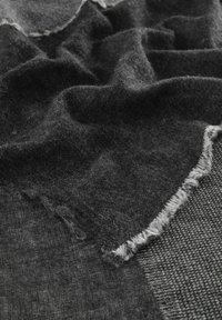 Tissu gris foncé avec des textures variées, présentant un bord effiloché et un tissage à motifs. Apparence douce et drapée.