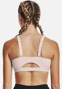 Mujer con el cabello trenzado vista desde atrás, que lleva un sujetador deportivo rosa claro con tirantes ajustables y un corte debajo del broche.
