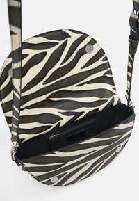 Zebrastreifen-Umhängetasche aus Kunstleder mit abgerundetem Überschlag und magnetischem Druckverschluss, innen mit dunklem Stofffutter und Reißverschlusstasche.