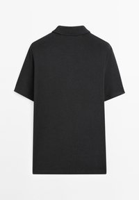 Černá polo košile vyrobená z texturované bavlny, s klasickým límcem, krátkými rukávy a volným střihem, pohled zezadu.