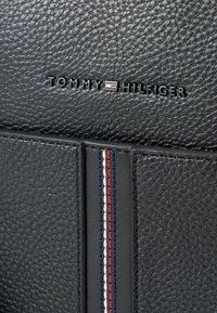 Μαύρο υφασμάτινο δερμάτινο προϊόν με το λογότυπο "TOMMY HILFIGER". Διακριτή διακοσμητική ραφή σε κόκκινες, λευκές και μπλε κάθετες ρίγες.