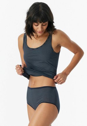 Woman wearing navy and gray striped tank top and matching high-waist underwear, adjusting her shirt, against a plain white background.