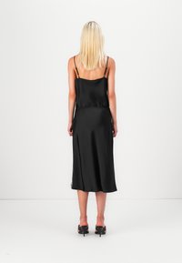 Musta satiini mekko ohuilla olkaimilla, keskipitkä, jossa on sileä pinta ja pitsikoriste helman reunassa. Minimalistinen muotoilu ja siluetti.