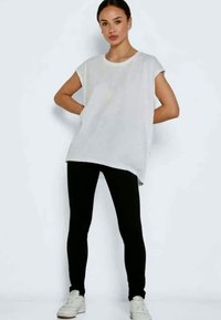 Fehér, oversized póló rövid ujjakkal, fekete leggingsszel és fehér sportcipővel párosítva. Egyszerű, hétköznapi dizájn, puha textúrával.