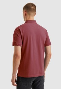 Polo majica s kratkimi rokavi v maroon barvi iz bombaža, ki ima klasičen ovratnik, žep na levi manšeti in raven rob.