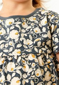 Ein Kind trägt ein dunkelblaues Kleid mit weißen und gelben Blumenmustern und kurzen Ärmeln, das die Brust- und Halspartie zeigt.