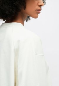 Ανοιχτόχρωμο φούτερ με μαλακή υφή, που διαθέτει άνετη εφαρμογή, στρογγυλή λαιμόκοψη και εμφανή ραφή κατά μήκος της ραφής του ώμου.