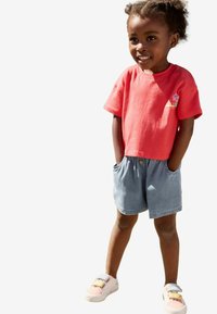 Koralfarvet t-shirt med korte ærmer og blomster-graphic, sammen med lyseblå denimshorts og hvide sneakers med pastelnuancer.