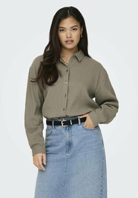 Olivgrünes Button-up-Hemd aus strukturiertem Stoff, mit langen Ärmeln und Kragen. Kombiniert mit einem hoch taillierten Jeansrock.