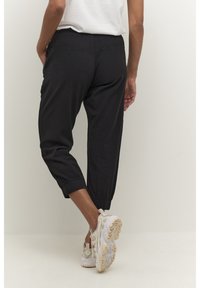 Zwarte cropped broek met een elastische tailleband en taps toelopende boorden, gemaakt van een lichte stof. Draag met witte en beige sneakers.