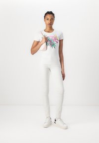 T-shirt blanc avec un imprimé floral coloré, design ajusté. Jean blanc, associé à des baskets blanches avec des accents noirs. Sac à main rose clair.