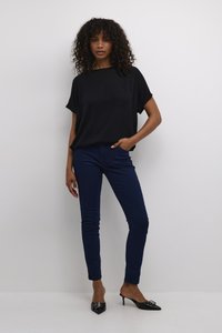 Black loose-fitting top, dark blue skinny jeans, and black pointed-toe heels with an embellishment, on a plain background.