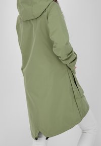 Ljus olivgrön parka med huva, sidofickor och en strömlinjeformad design. Tillverkad av ett glansigt, hållbart material.