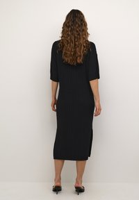 Abito midi nero a coste con maniche corte, fessure laterali e vestibilità comoda, realizzato in un morbido tessuto a maglia. Texture liscia e colore uniforme.