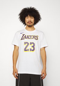 Hvid bomulds T-shirt med "LAKERS" i gul og lilla tekst over nummer "23". Korte ærmer og rund halsudskæring; Nike-logo på skulderen.