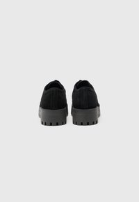 Chaussures en suède noir à profil bas, dotées d'une semelle en caoutchouc noir texturé et d'un arrière arrondi. Design simple sans matériel ni accents visibles.
