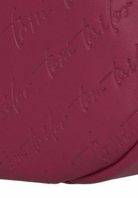 Bolso de cuero fucsia con patrón de logo en relieve "tom tailor", textura suave, forma redondeada y detalles de costura sutiles.