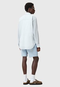 Camicia a maniche lunghe a righe azzurro chiaro, pantaloni corti in denim, calze bianche e sandali marroni. Vestibilità slim con orlo curvo e polsini con bottone.