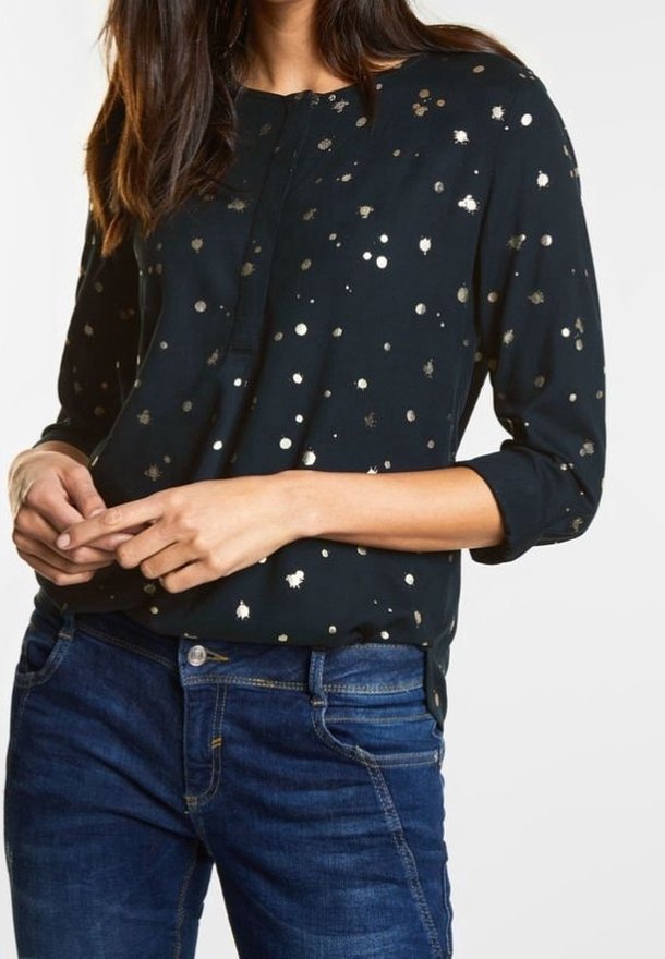 Svart blus med gyllene prickar, långärmad med uppkavlade ärmar, knappslå, lätt tyg, bärs tillsammans med blå jeans.
