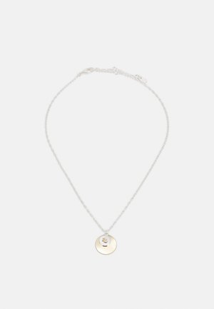 Collier en chaîne argentée avec un pendentif rond en or présentant un petit motif de couronne découpée au centre.