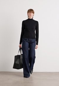 Fekete, hosszú ujjú felső sötétkék, bő szárú farmernadrággal párosítva; egy nagy fekete táska tartása. Minimalista design, sima textúrákkal.