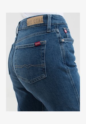 Tamsiai mėlyni džinsai su vidutinio aukščio juosmeniu, su odiniu juosmens etiketė ir kontrastinėmis siūlėmis ant galinių kišenių.