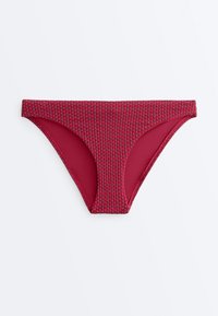 Bas de bikini rouge en tissu texturé avec de petits points en relief, sur un fond blanc uni.