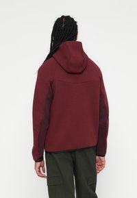 Sweatshirt capuz bordeaux com uma textura suave, apresentando painéis laterais em um tom mais escuro e um ajuste relaxado e ajustado.