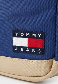Sötétkék hátizsák texturált anyagból. Yalap alakú logó folt található rajta "TOMMY JEANS" felirattal, piros, fehér és kék díszítéssel.