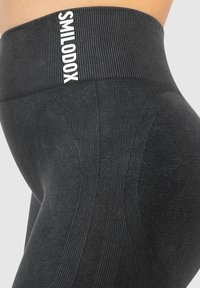 Czarnie legginsy z wysokim stanem, z prążkowanym pasem, bezszwowym wzorem, teksturowanym materiałem i kontrastowym białym logo na pasie.