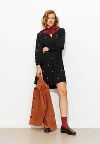 Robe noire avec broderies florales, manches longues bouffantes et taille cintrée. Un manteau en suède marron et des chaussettes bordeaux complètent la tenue.