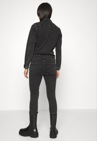 Combinaison en denim noir à silhouette ajustée, col plat et manches longues ; dotée d'une poche arrière et de bottes en cuir noir assorties.
